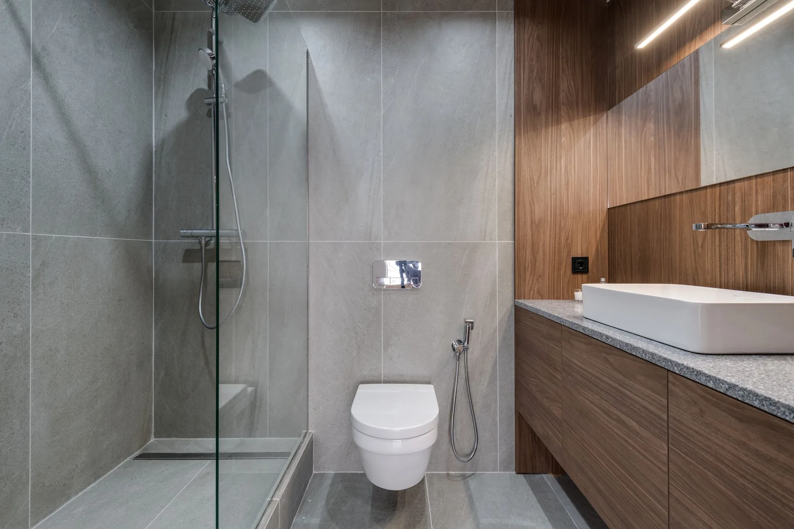 A modern bathroom with grey tiles, a walk-in shower, wall-hung toilet and vanity unit
