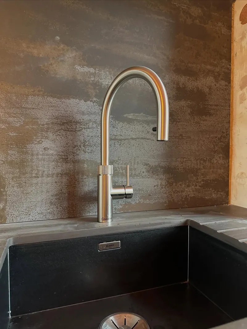 A brushed brass kitchen tap over a sink, fitted by Addisons