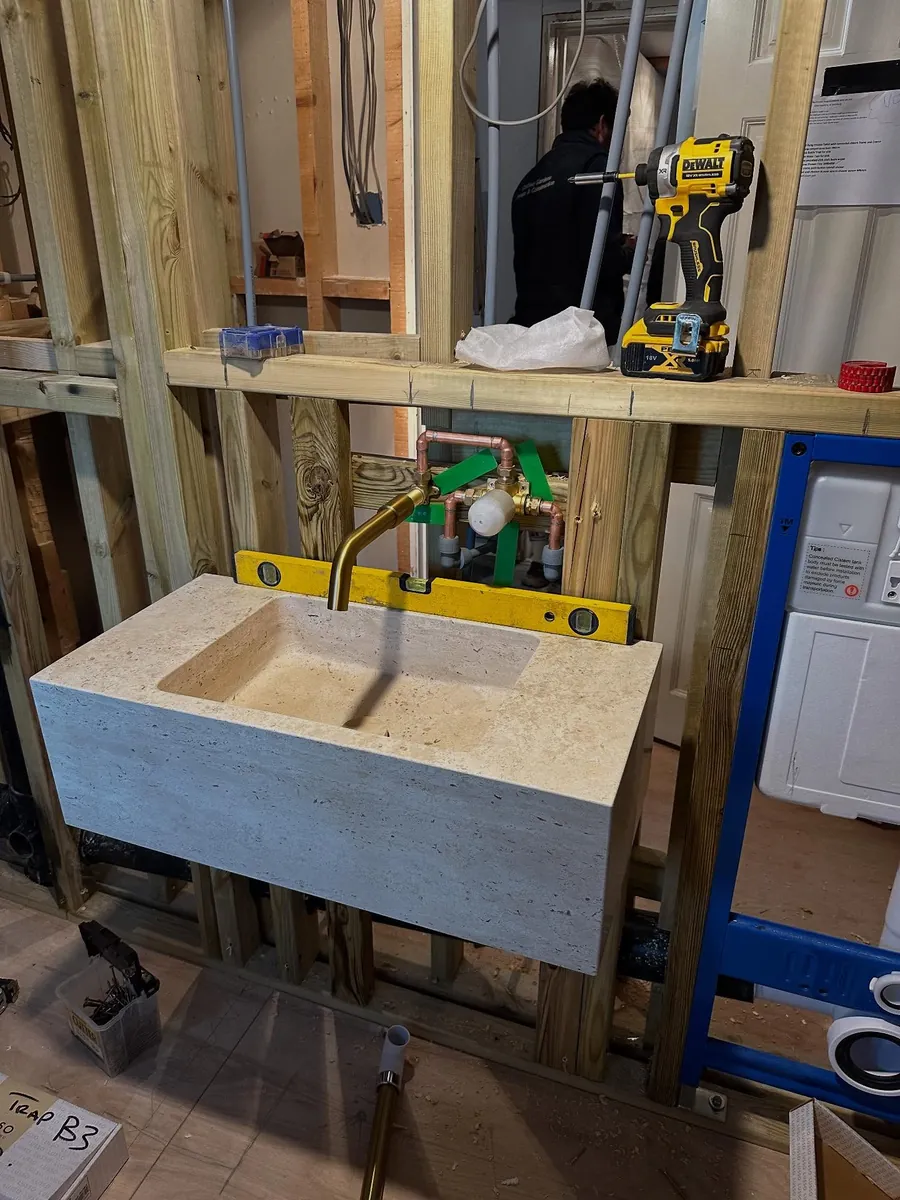 Mid-job: a stone basin being fitted to a new stud wall, with the level, drill and copper pipework out