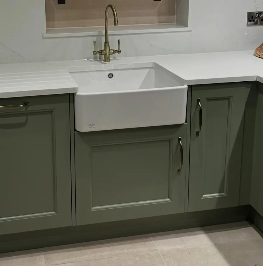 A white Belfast sink with a brass tap in a sage green kitchen, plumbed by Addisons