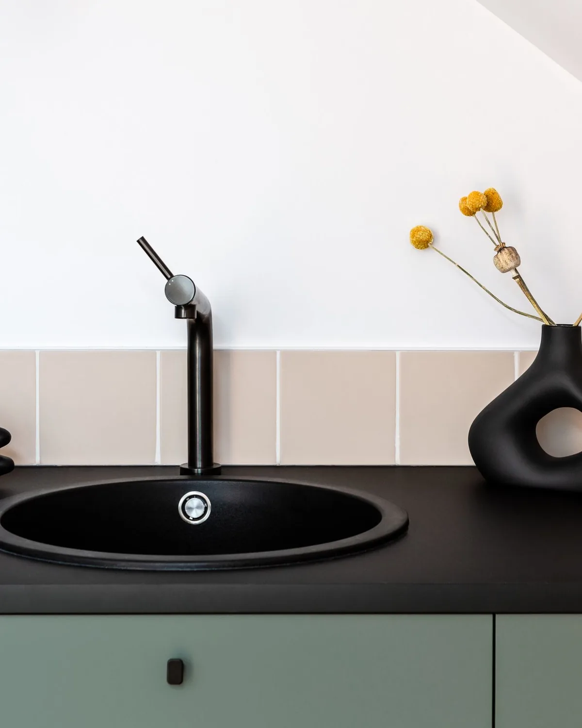 A modern sage green kitchen with a round black sink and mixer tap set into the worktop
