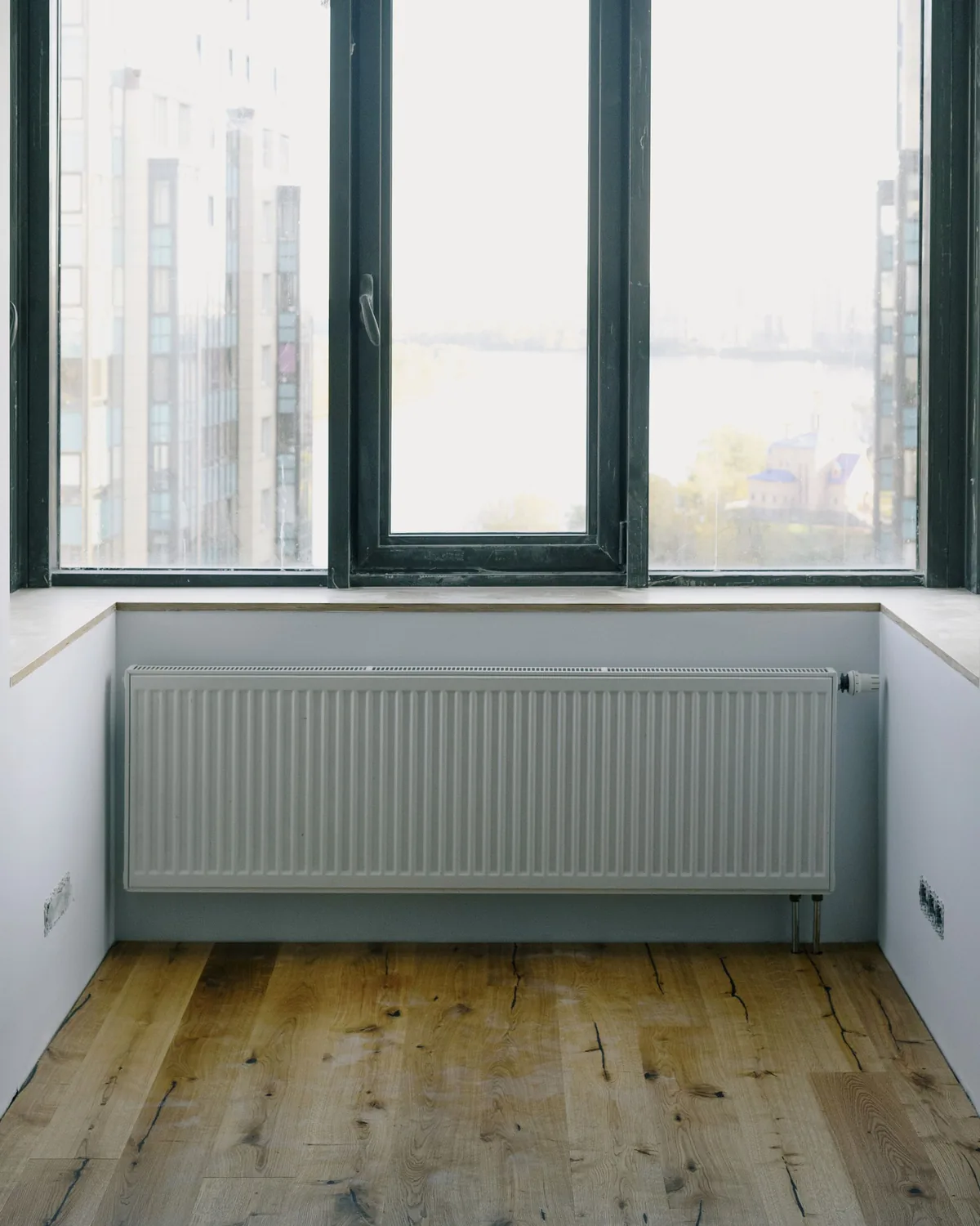 A white panel radiator fitted under a window in a bright room