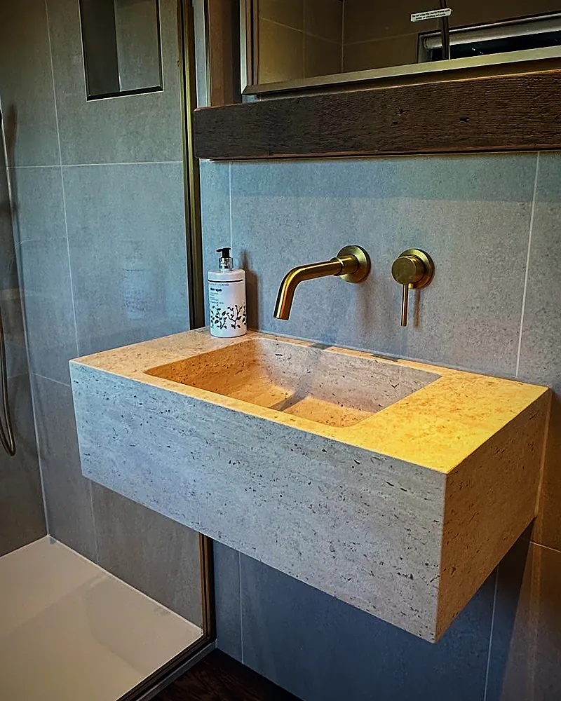 Brushed brass wall-mounted taps over a stone basin, fitted by Addisons